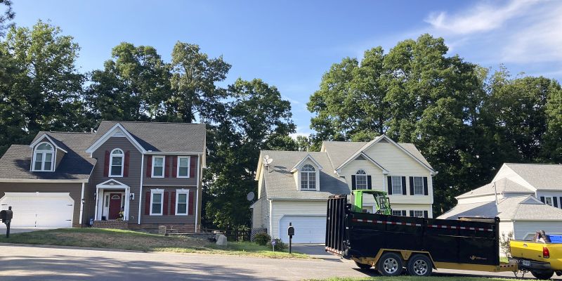 Long Shot Of Houses Having Trees Behind Them And A Roadway With A Parked Dump Vehicle And A Park Beside The Road