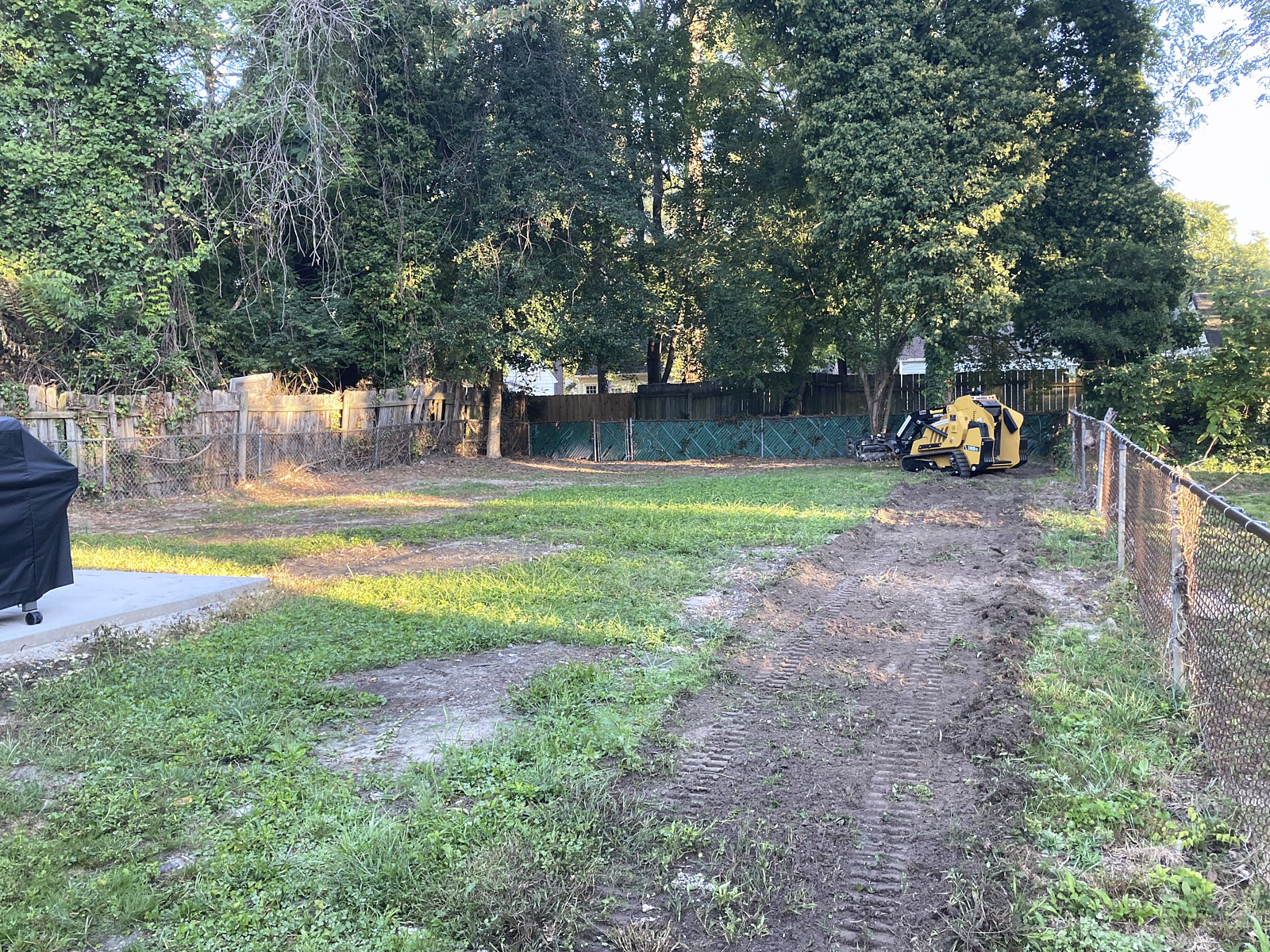 A Yellow Mini Skid Steer Working In A Big Green Lawn For Mulching And Grading The Sand After Tree Stump Removal